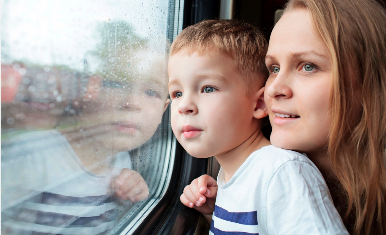 Tunnelmallisessa kuvassa äiti ja alakouluikäinen nuori poika katselevat maisemaa junan ikkunan läpi. Pojan kasvot heijastuvat kuvajaisena ikkunalasista.
