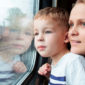 Tunnelmallisessa kuvassa äiti ja alakouluikäinen nuori poika katselevat maisemaa junan ikkunan läpi. Pojan kasvot heijastuvat kuvajaisena ikkunalasista.